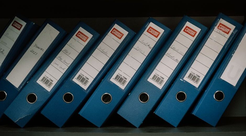 Neatly arranged blue office binders labeled with dates and names for organized storage.