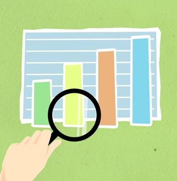 Top view of decorative cardboard illustration of hand with magnifying glass above diagram with columns on green background