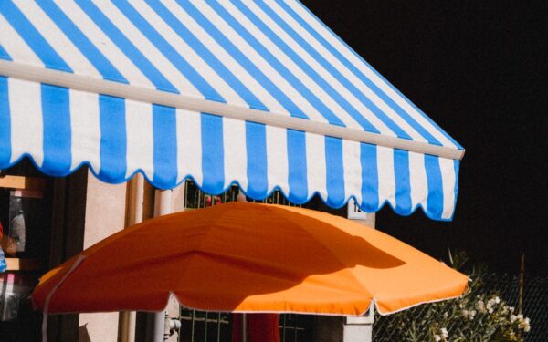Vibrant blue striped awning and orange umbrella providing summer shade outdoors.