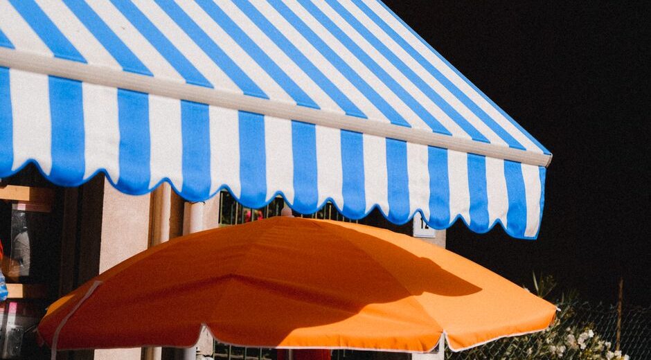 Vibrant blue striped awning and orange umbrella providing summer shade outdoors.