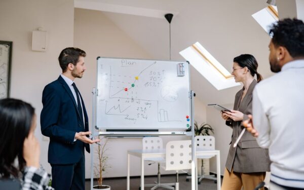 Colleagues collaborating at a business meeting, analyzing graphs on a whiteboard.