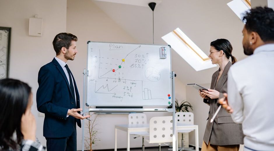 Colleagues collaborating at a business meeting, analyzing graphs on a whiteboard.